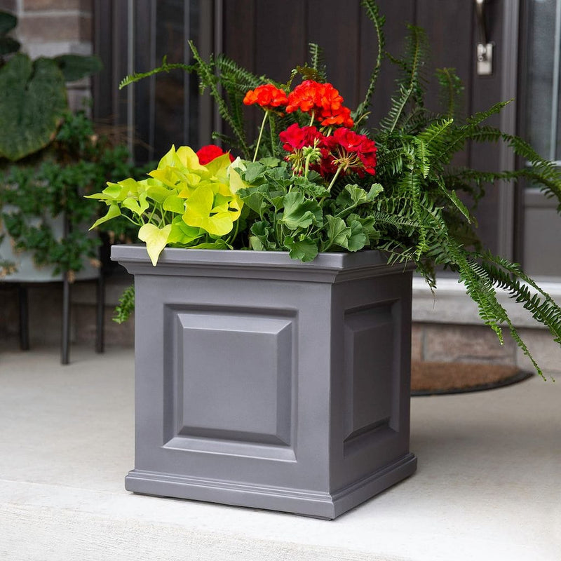 The Mayne Nantucket Square Planter, in the graphite finish,planted with seasonal annuals, decorating a patio.