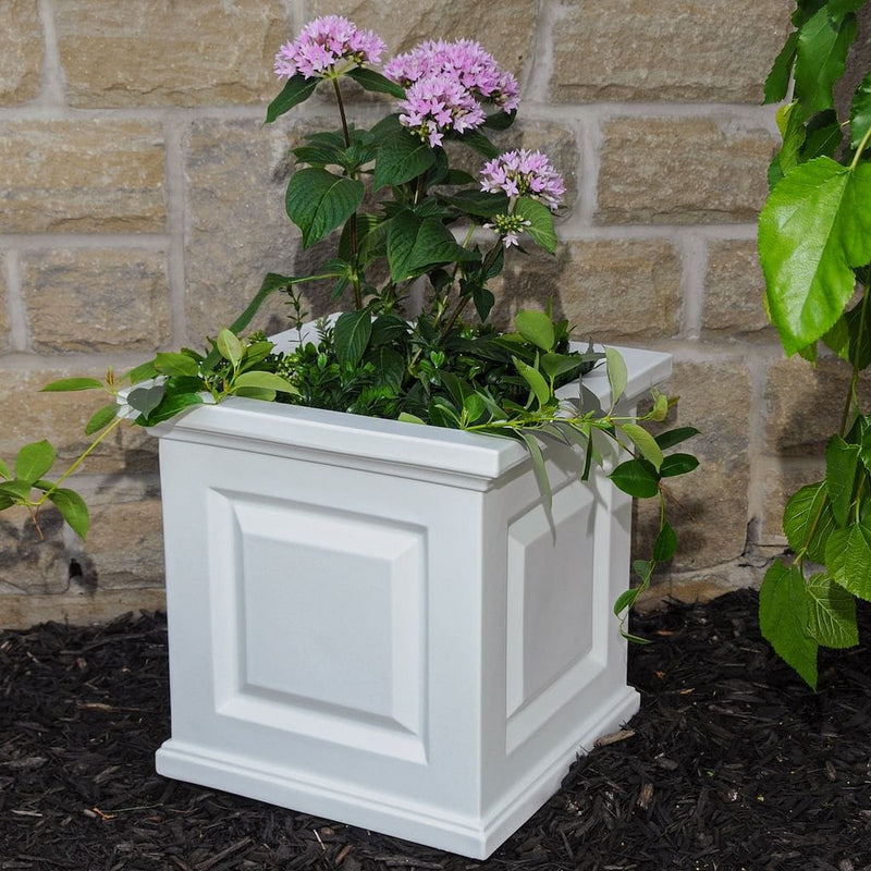 The Mayne Nantucket Square Planter, in the white finish, planted with seasonal annuals, decorating a patio.