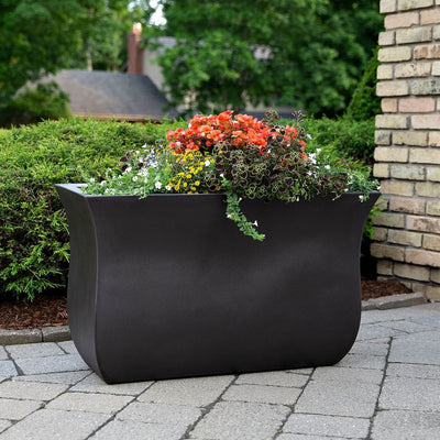 The Mayne Valencia Long Planter, in the espresso finish, planted with soft foliage and placed in the garden.
