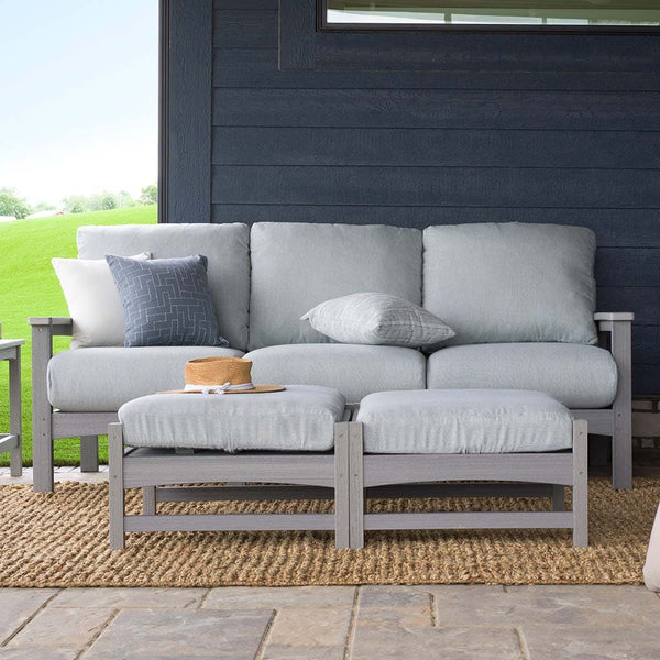 Camden Sofa by Berlin Gardens set on an outdoor patio, featuring a grey frame with white cushions, accompanied by an ottoman with a similar color scheme.