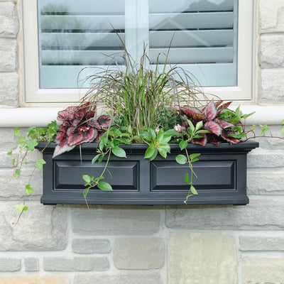 The Mayne Nantucket 3ft Window Box Planter, with a black finish, mounted under a window and filled with colorful flowers.