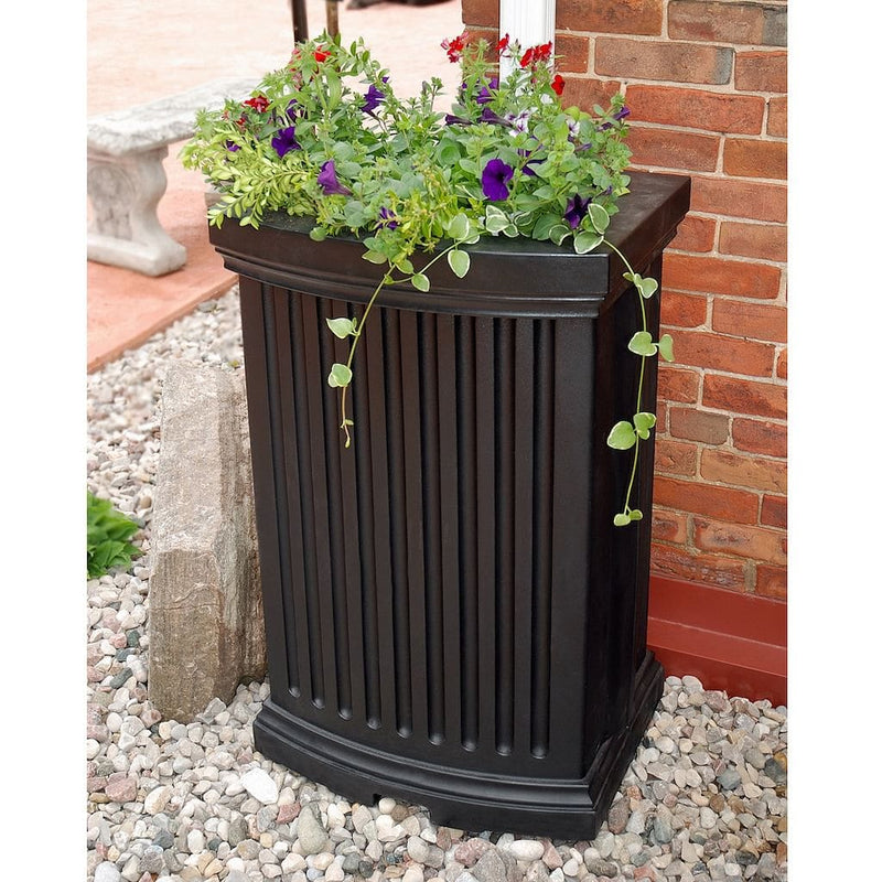 The Mayne Madison Rain Catcher in Black, in the black finish, installed next to house and planted with colorful flowers.