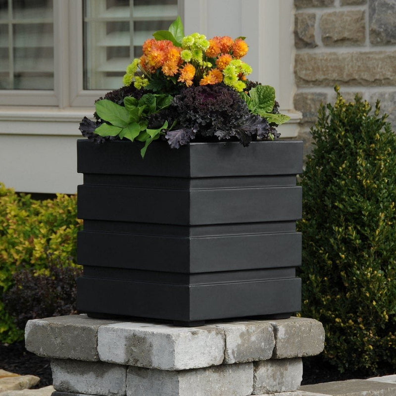 The Mayne Freeport 18x18 Square Planter, in the black finish, simply planted with flowers to add curb appeal to a front entry of a home.