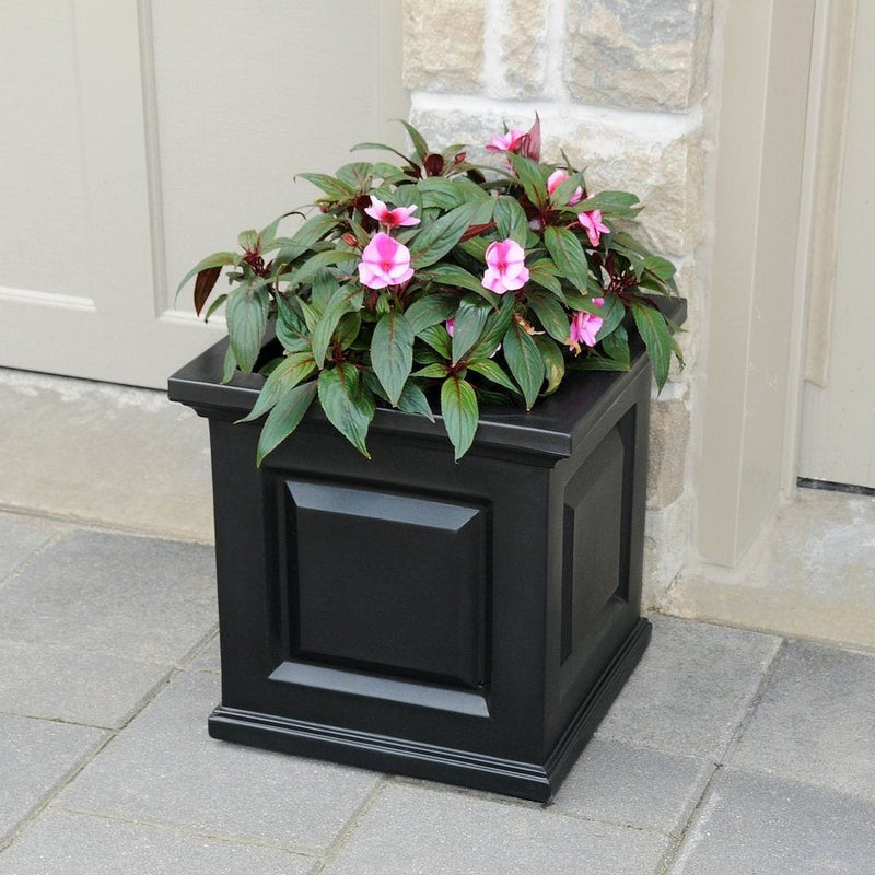 The Mayne Nantucket Square Planter, in the black finish, planted with cool season annuals, decorating a patio.