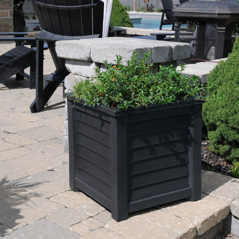 The Mayne Lakeland 20x20 Square Planter, in the black finish, planted with cool season annuals, decorating a patio.