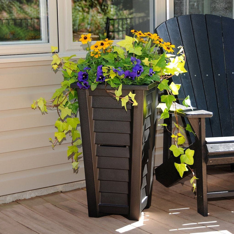 The Mayne Lakeland 28 inch Tall Planter, in the black finish, planted with cool season annuals, decorating a patio.