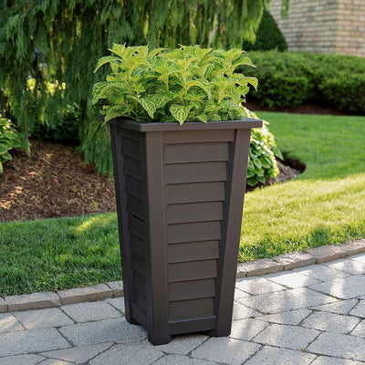 The Mayne Lakeland 28 inch Tall Planter, in the espresso finish, filled with soft foliage for a patio.