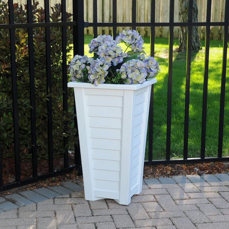 The Mayne Lakeland 28 inch Tall Planter, in the white finish, filled with shade flowers and placed on a garden patio.