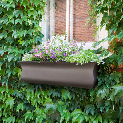 The Mayne Valencia 3ft Window Box Planter, with a espresso finish, mounted under a window and filled with colorful flowers.