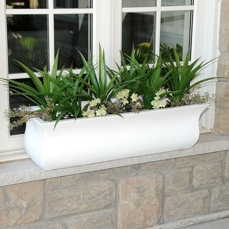 The Mayne Valencia 3ft Window Box Planter, with a white finish, mounted under a window and filled with colorful flowers.