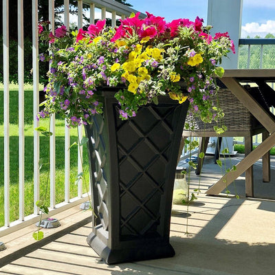 The Mayne Georgian Tall Planter, in the black finish, planted with colorful annuals and placed on a sunny deck.