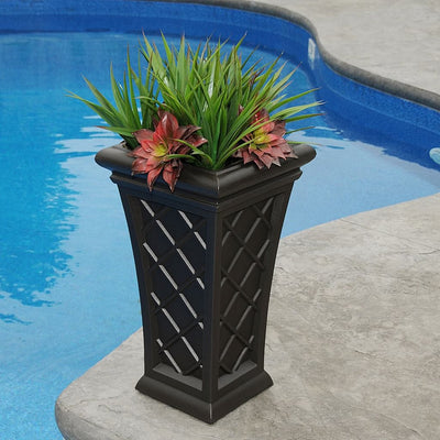 The Mayne Georgian Tall Planter, in the espresso finish, filled with tropical plants and set pool side.