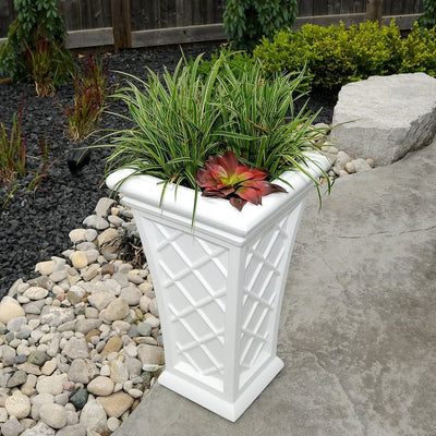 The Mayne Georgian Tall Planter, in the white finish, filled with foliage and placed on a sunny patio.