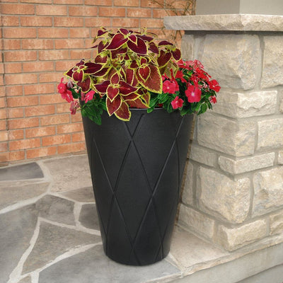 The Mayne Versailles Tall Round Planter, in the black finish, planted with colorful flowers and placed on a patio