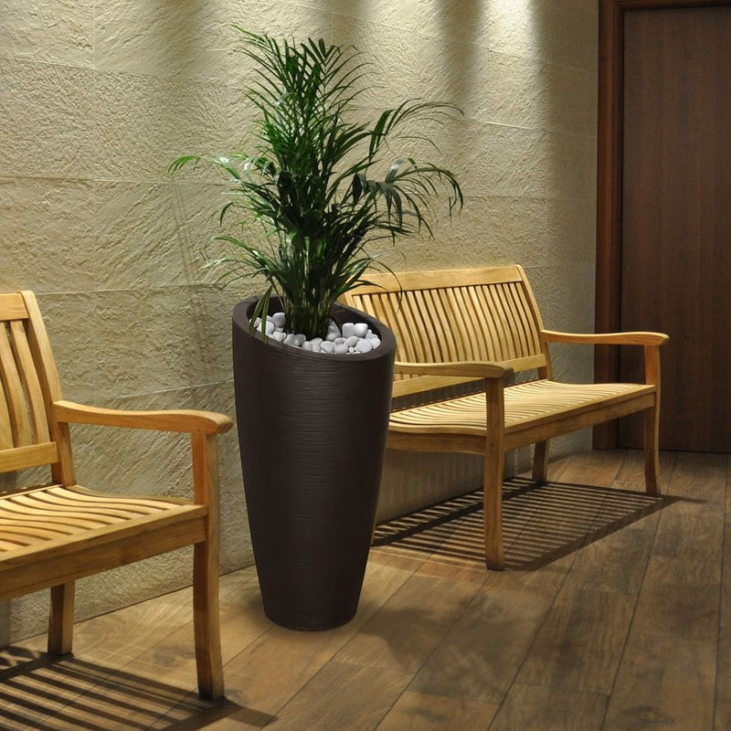 The Mayne Modesto Tall Planter, in the espresso finish, is holding a palm and accenting a seating area in an indoor office building.