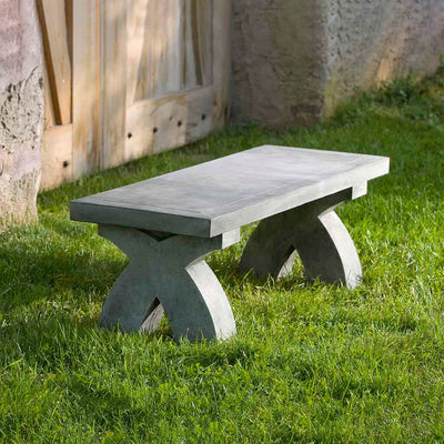 Campania International The X Bench, set in the garden to adding charm and purpose. The bench is shown in the Alpine Stone Patina.