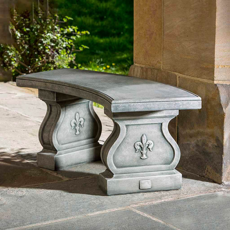 Campania International Fleur De Lys Curved Bench, set in the garden to adding charm and purpose. The bench is shown in the Alpine Stone Patina.