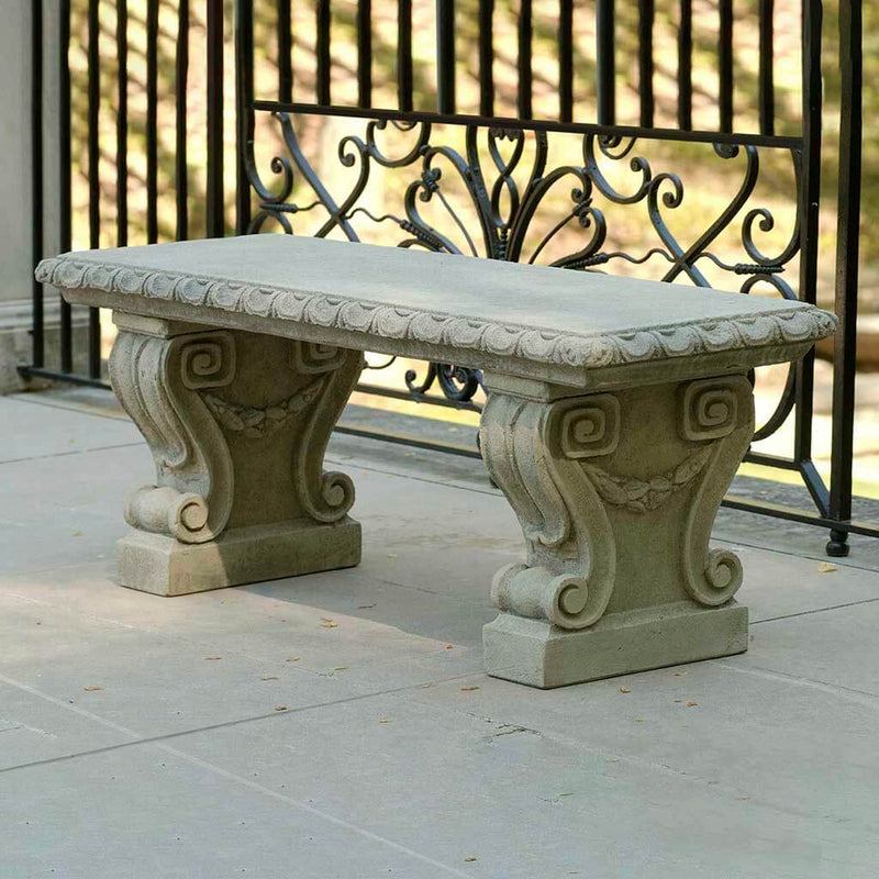 Campania International Longwood Main Fountain Garden Bench, set in the garden to adding charm and purpose. The bench is shown in the Greystone Patina.