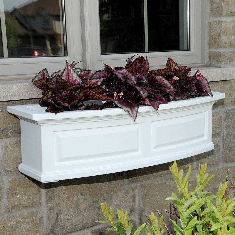 The Mayne Nantucket 3ft Window Box Planter, with a white finish, mounted under a window and filled with colorful flowers.