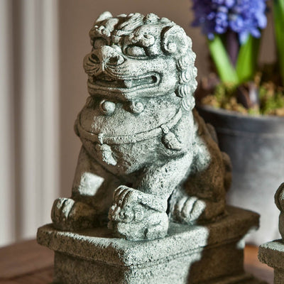 Campania International Small Temple Foo Dog Left Dog Statue, set in the garden to adding charm an meaning. The statue is shown in the Alpine Stone Patina.