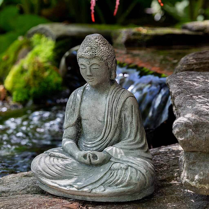 Campania International Small Buddha Statue, set in the garden to adding charm an meaning. The statue is shown in the Alpine Stone Patina.