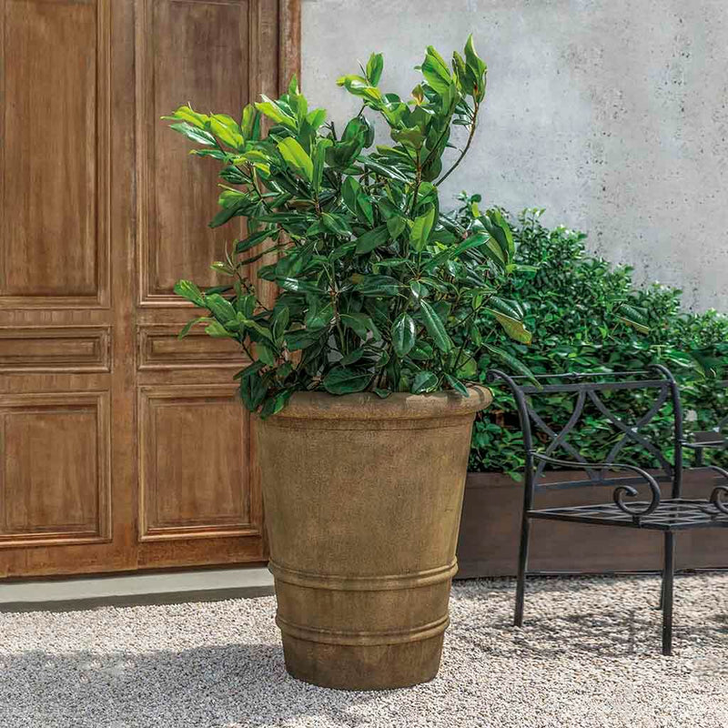 Campania International Urbino Extra Large Planter, a tall classic planter filled with foliage, shown in the Age Limestone Patina. Made from cast stone.