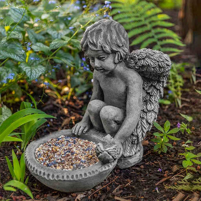 Campania International Cherub Birdfeeder Statue placed in the garden. Religious garden statues, made of cast stone in a range of color options.