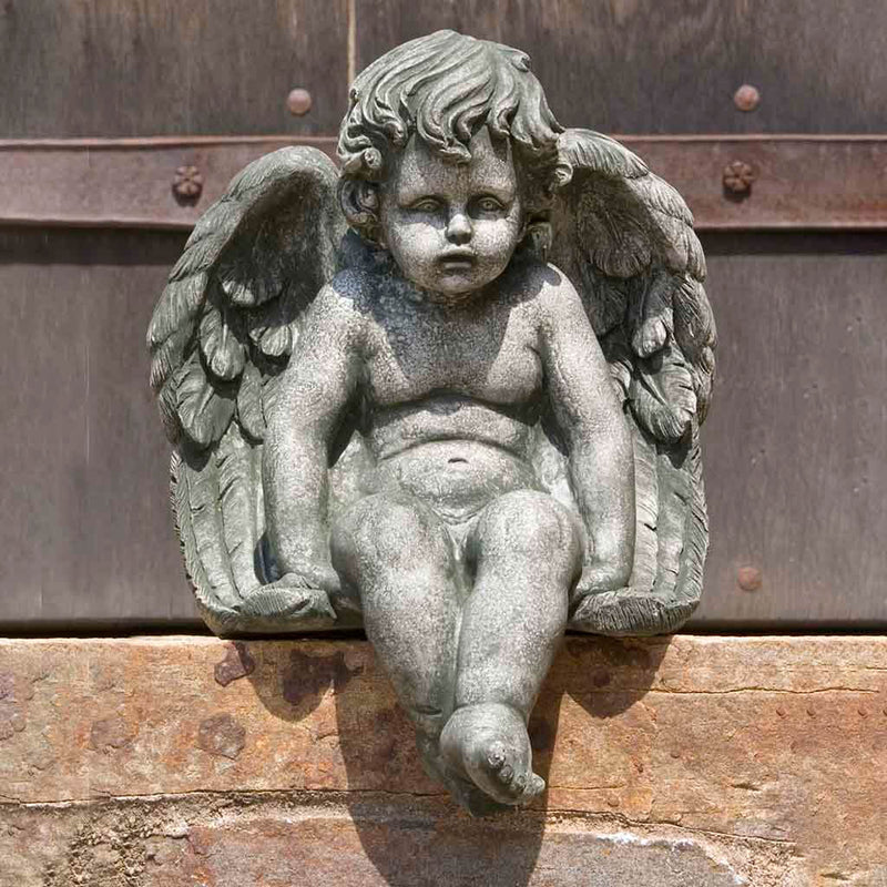 Campania International Medium Sitting Cherub Statue placed in the garden. Religious garden statues, made of cast stone in a range of color options.