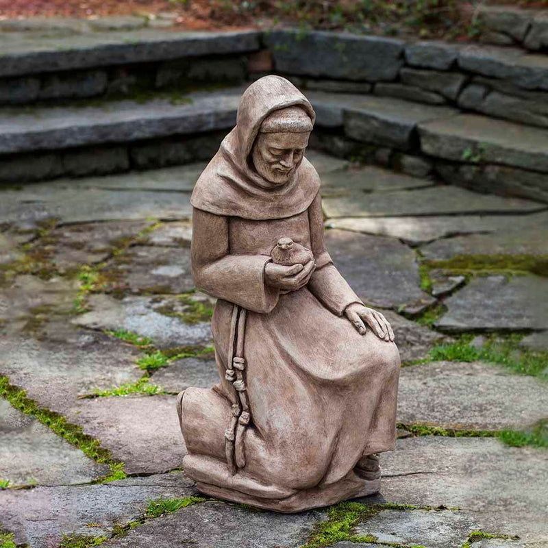 Campania International Kneeling St. Francis with Bird Statue placed in the garden. Religious garden statues, made of cast stone in a range of color options.